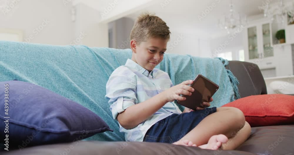 Happy caucasian boy at home, sitting on couch using tablet, playing game and smiling Happy caucasian boy at home, sitting on couch using tablet, playing game and smiling
