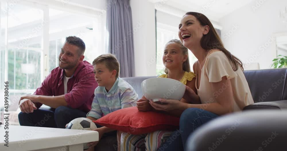 Excited caucasian parents, son and daughter on couch watching tv and cheering, son holding football Excited caucasian parents, son and daughter on couch watching tv and cheering, son holding football