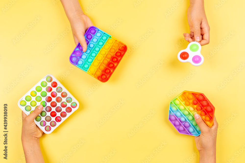 Obraz premium Many hands holding colorful pop it fidget toys on yellow background. Push pop-it fidgeting game helps relieve stress, anxiety, autism, provide sensory and tactile experience for children