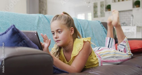 Happy caucasian girl at home, lying on couch using tablet and smiling