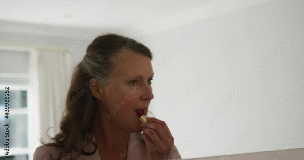 Senior caucasian woman standing in room looking in mirror and putting on lipstick Senior caucasian woman standing in room looking in mirror and putting on lipstick