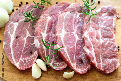 Sliced raw pork meat with fresh rosemary, onion, pepper and garlic on cutting board