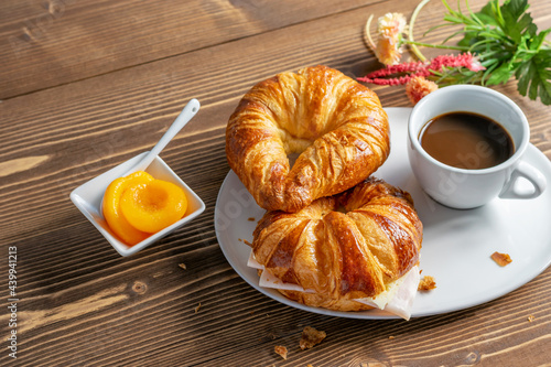 French croissants, cup of coffee and peach jam on the wooden table. Tasty breakfast with coffee and croissant with ham and cheese. Gourmet eating, country morning.