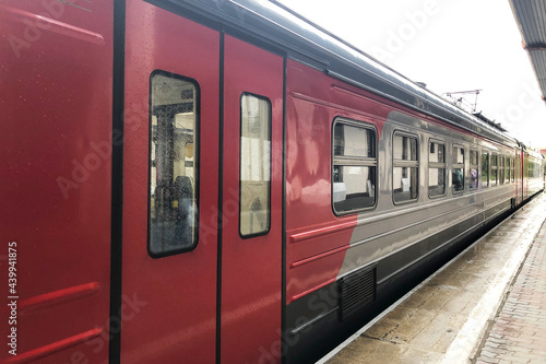 Red and grey train wagon stand near platform on train station with closed doors.