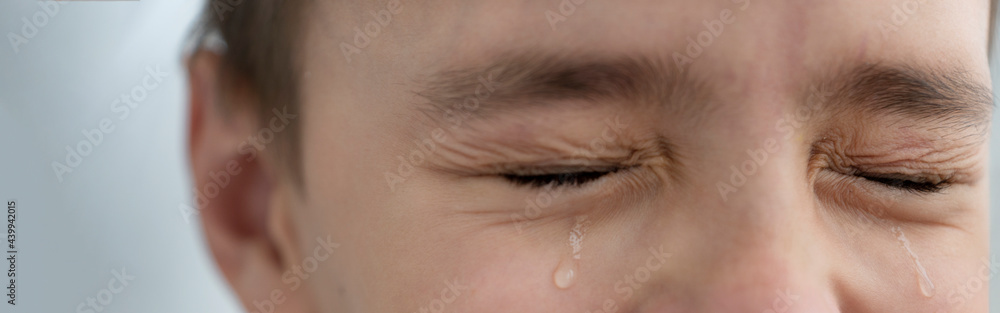 Obraz premium Teardrops rolls down the boy's cheeks, his eyes are closed, he is upset and crying. Sad, unhappy emotions of child, banner size.