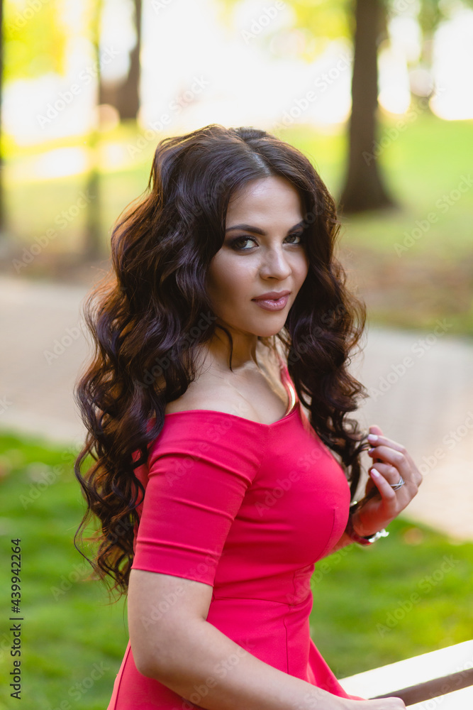 Close-up portrait of a beautiful young girl with long dark wavy hair in a red dress in the park at sunset Close-up portrait of a beautiful young girl with long dark wavy hair in a red dress in the park at sunset