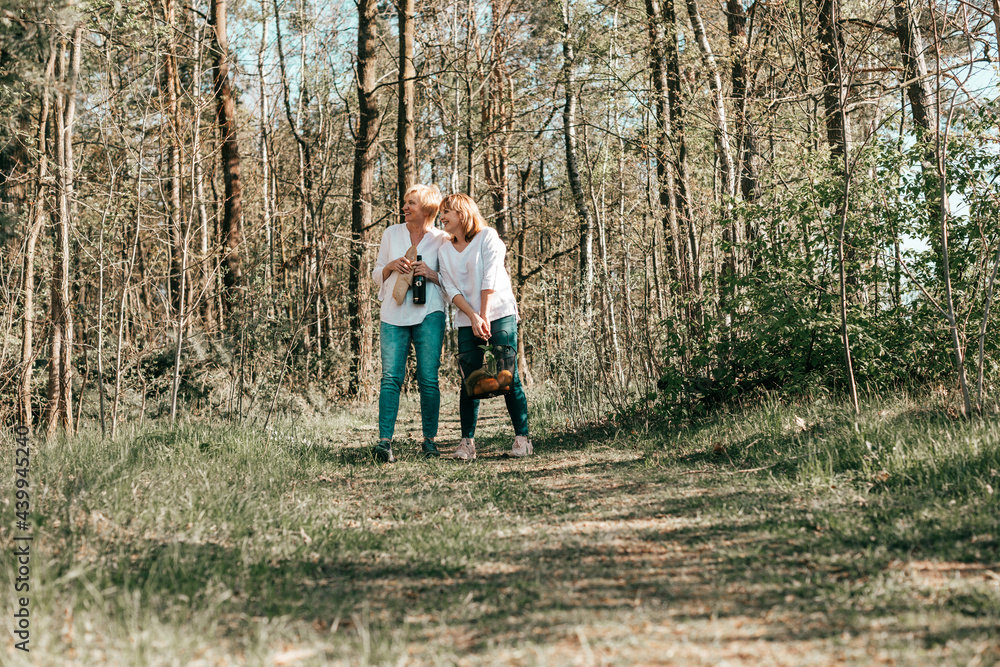 Fototapeta premium Two female friends mature are walking through forest. Active lifestyle, hobby