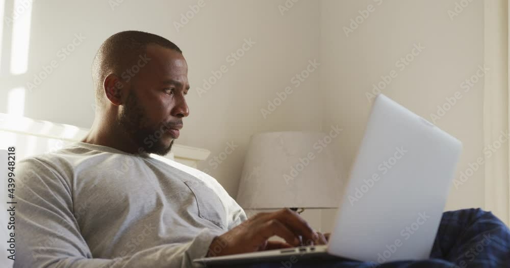 African american man using laptop while sitting on the bed at home African american man using laptop while sitting on the bed at home