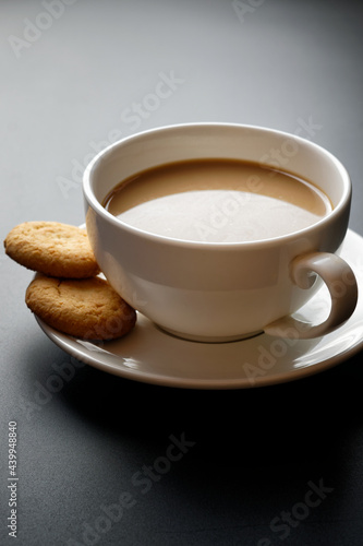 Latte in white coffee cup, with two cookies on the saucer. On black background in backlight.