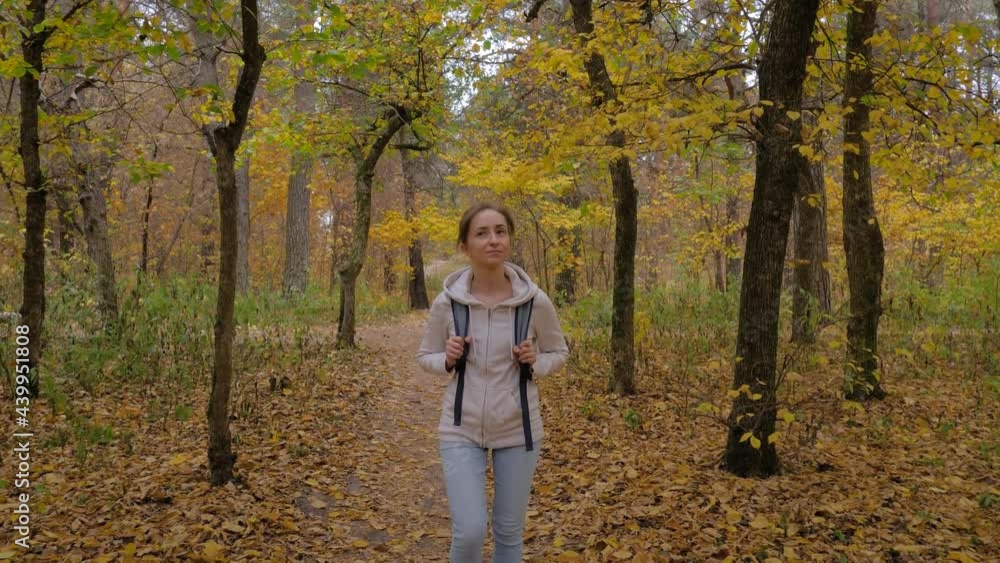 Front view of young positive woman with backpack walking in autumn park, forest and looking around - wide angle steadicam shot. Active outdoor lifestyle, leisure time, freedom and adventure concept Front view of young positive woman with backpack walking in autumn park, forest and looking around - wide angle steadicam shot. Active outdoor lifestyle, leisure time, freedom and adventure concept