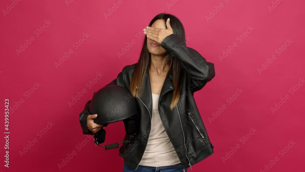 Young woman holding a motorcycle helmet covering eyes by hands. Surprised to see what is ahead over isolated background Young woman holding a motorcycle helmet covering eyes by hands. Surprised to see what is ahead over isolated background