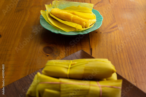 Uma porção de pamonhas amarradas na palha de milho e uma pamonha aberta e pronta para o consumo. photo