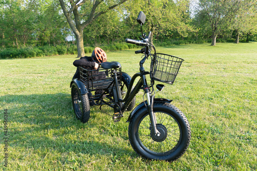 Fototapeta premium Woman in the hamlet hold the key of the electric bicycle battery pack. Female switch on the powered e bike with the key in the park in sunny summer day. The view of the e bike motor.