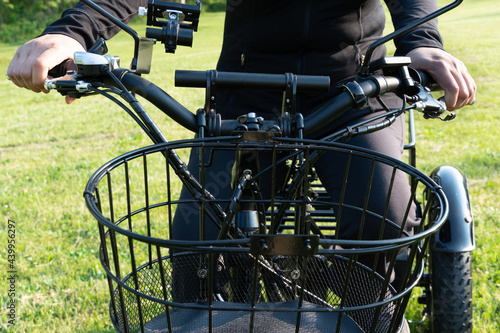 Woman riding electric bicycle in the park at summer day. Natural lighting. View of the front e bike side, electronics and wires. Summer leisure lifestyle.