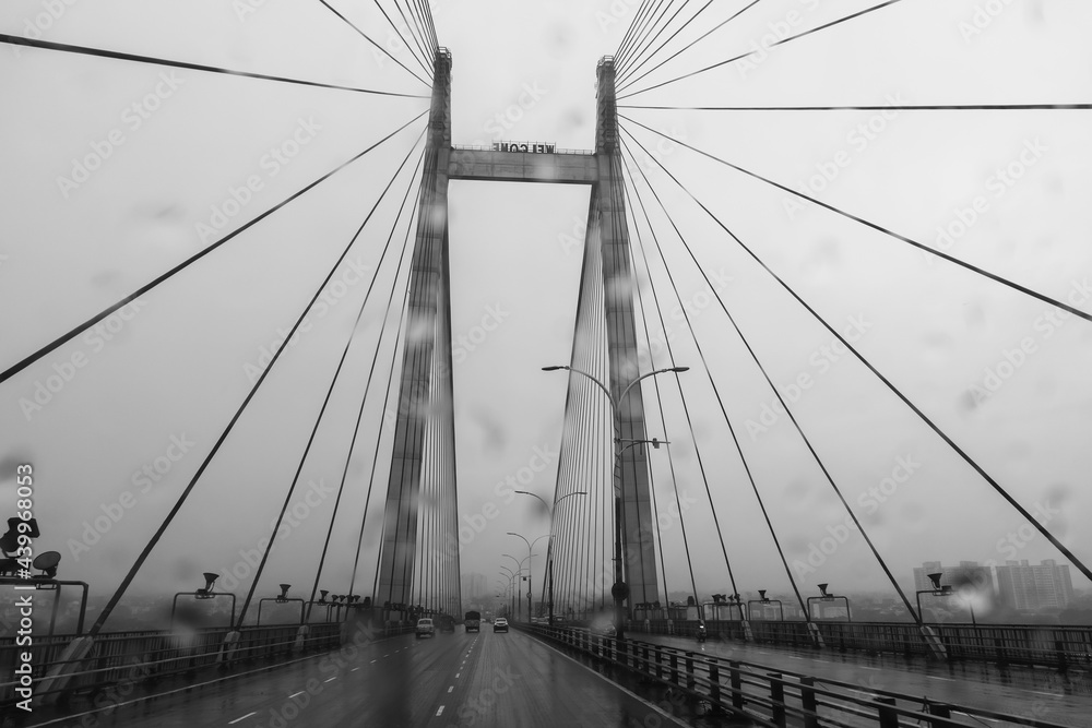 Naklejka premium Vidyasagar Setu over river Ganges, known as 2nd Hooghly Bridge in Kolkata,West Bengal, India. Abstract black and white image shot aginst glass with raindrops all over it, monsoon image of Kolkata.