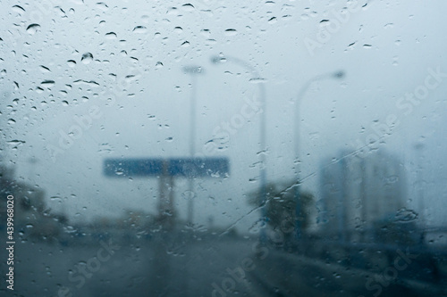 Raindrops falling on car windshield glass, abstract blurs of Nabanna building and road sign. Monsoon stock image of Howrah city , West Bengal, India photo