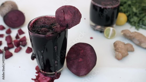 A glass of fresh beetroot beverage decorated with a slice splashing out. Closeup shot of fresh vegetables like lemon  ginger  a glass of juice kept against a white background - healthy eating photo