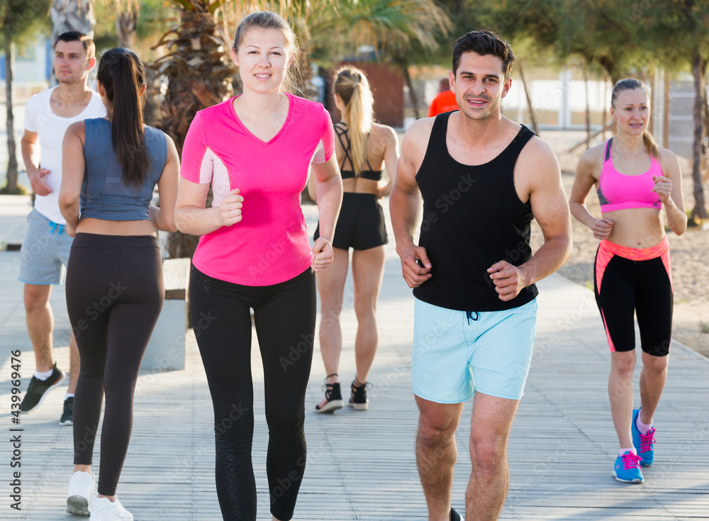 Obraz premium Sporty women and men running along embankment in sunny morning
