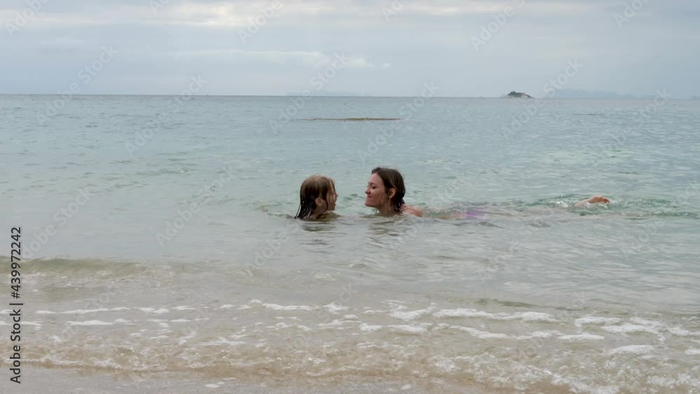 Mother and daughter swim in sea water in sunshine on summer day. Family vacations and travelling concept Mother and daughter swim in sea water in sunshine on summer day. Family vacations and travelling concept