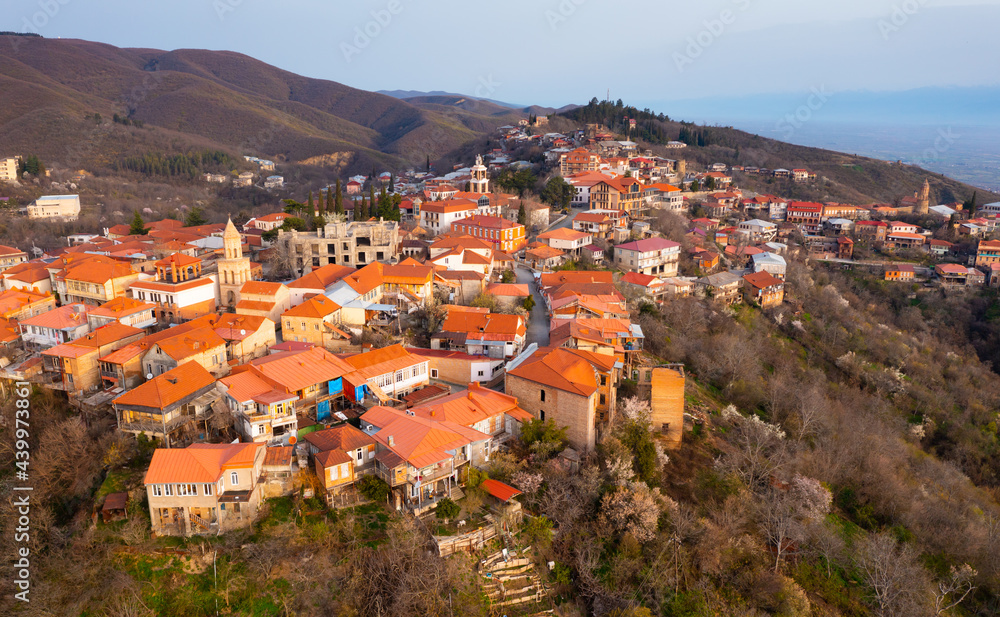 Picturesque aerial view of small Georgian town of Sighnaghi with similar terracotta roofs of houses on steep hill near Gombori Range on spring day, Kakheti, Georgia..