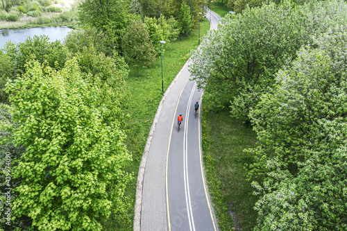 two cyclists ride bikes on bicycle path in city park at spring day. aerial photography with drone.