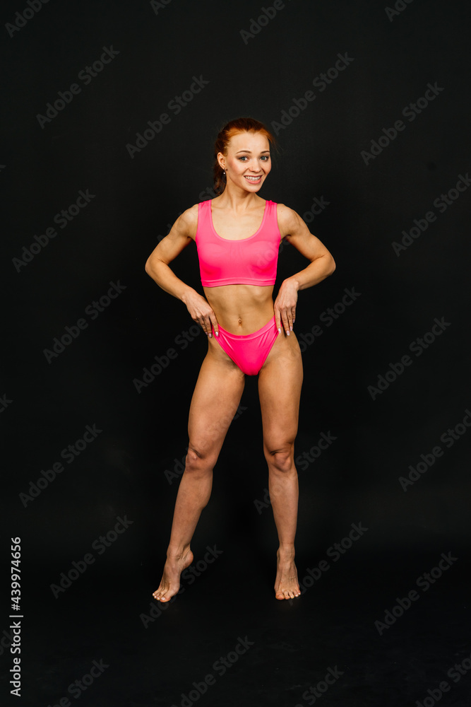 Beautiful young sporty muscular woman, isolated against dark background