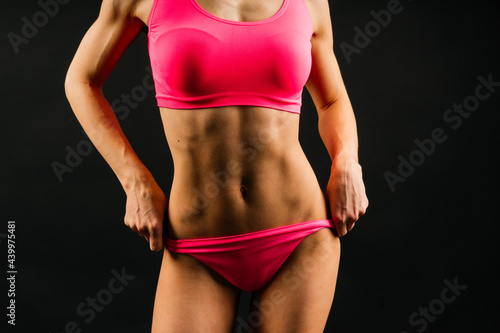 Beautiful young sporty muscular woman, isolated against dark background