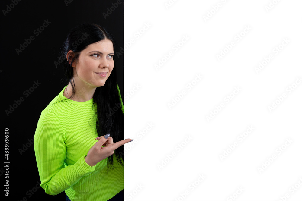 attractive dark-haired woman in bright colored clothes with a white blank poster, isolated on a dark attractive dark-haired woman in bright colored clothes with a white blank poster, isolated on a dark