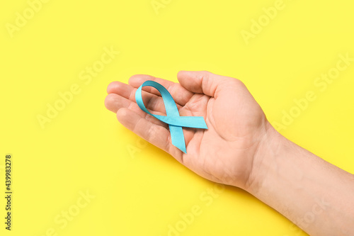 Male hand with light blue ribbon on color background. Prostate cancer concept