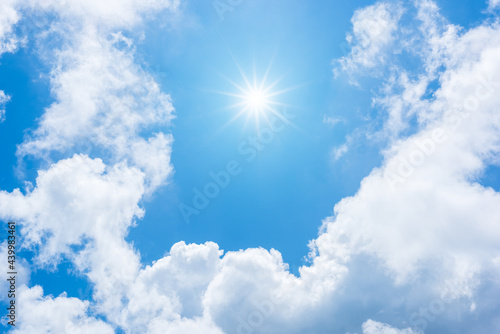 Sun with sunlight in white clouds on blue sky.