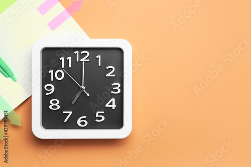 Stylish clock and notebook on color background