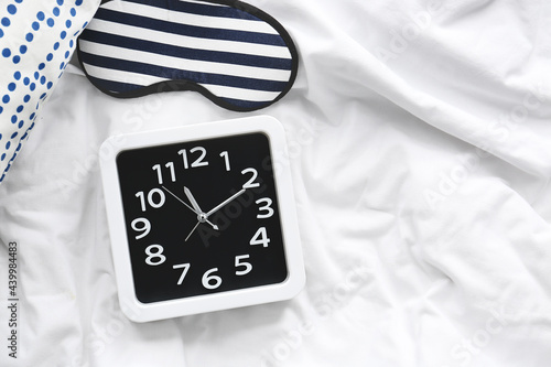 Stylish clock and sleeping mask on bed