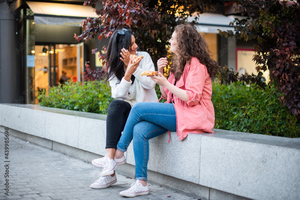two girls eating pizza in the city two friends sitting eating. Two tourist on the street eating. A lesbian couple eating together