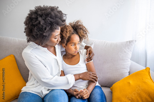 African American mother consoling her sad girl at home. Young black mother taking care of her depressed little daughter at home. Worried young foster mother comforting embracing adopted child daughter