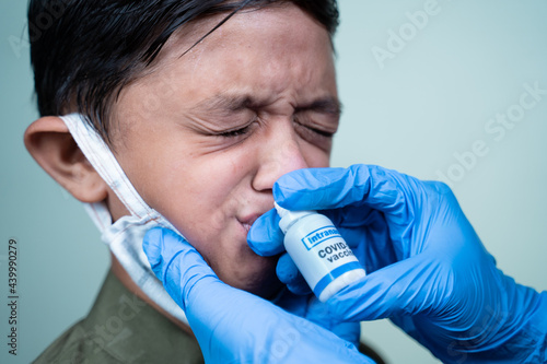 Head shot of child with medical face mask getting Intranasal Coronvirus covid-19 vaccination through nostril from doctor - concept of covid nasal vaccine
