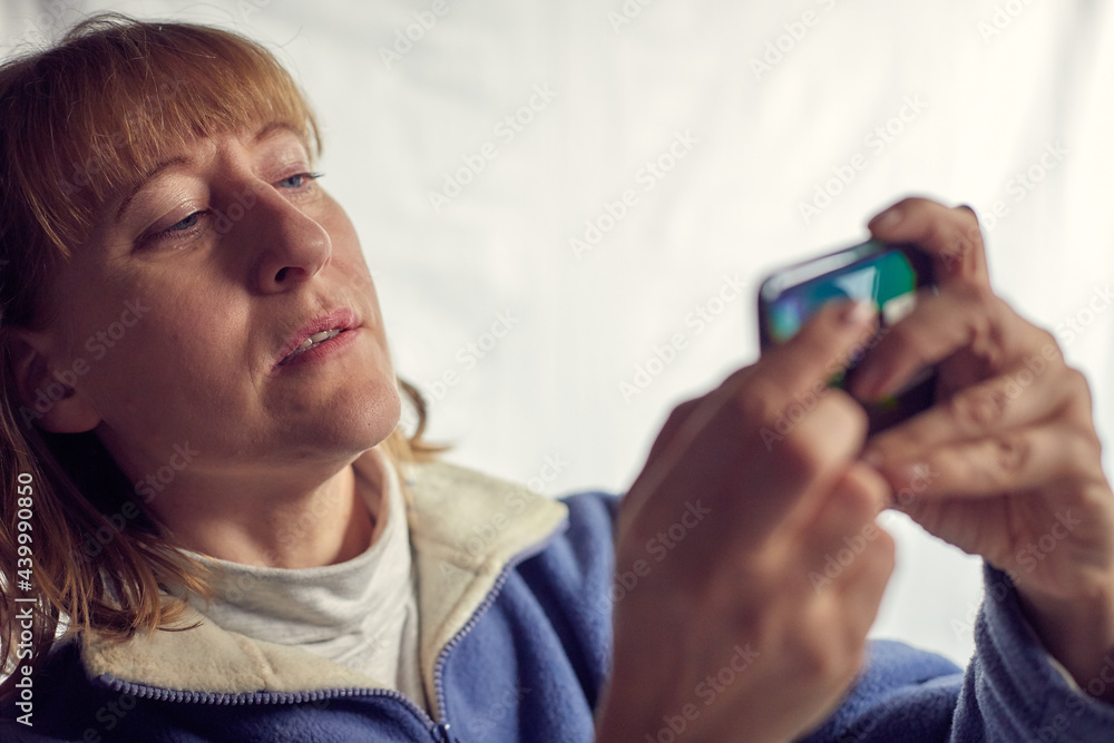 Fototapeta premium Portrait of a middle-aged woman with cell phone on a white background. Unprofessional female model doing selfie in the room or in the Studio