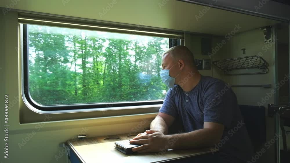 A man in a medical mask rides by the window on a train A man in a medical mask rides by the window on a train