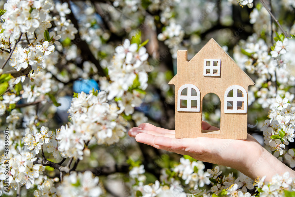 The girl holds the house symbol against the background of blossoming cherry The girl holds the house symbol against the background of blossoming cherry