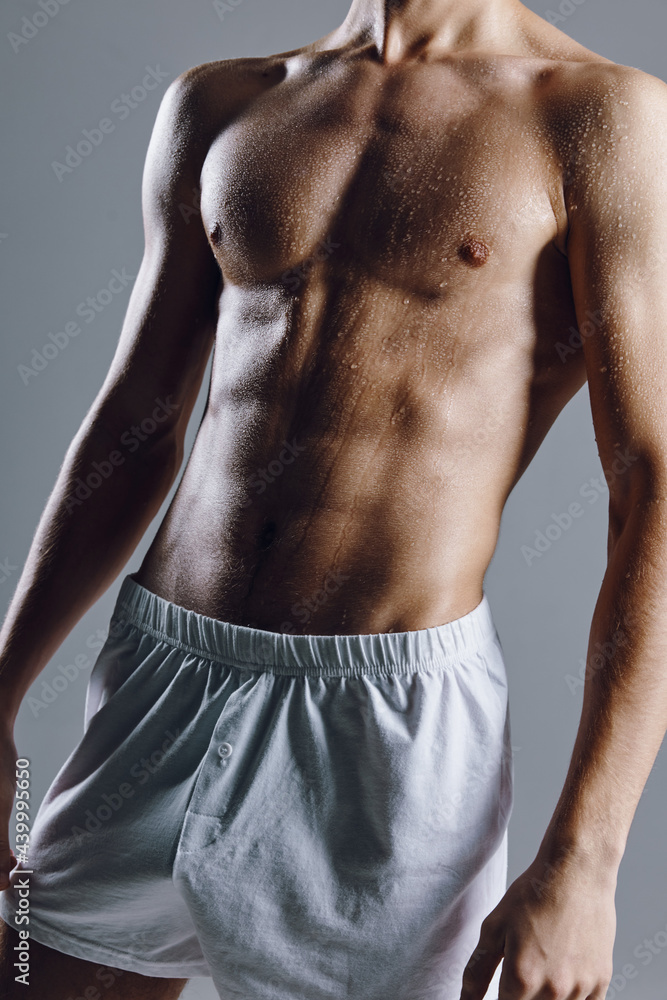 sporty male bodybuilder with abs cubes on stomach gray background white shorts 