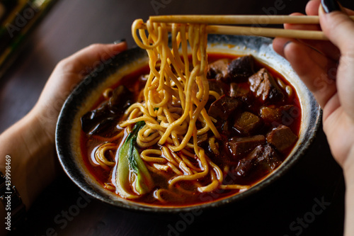 Young woman eating chineese soup with noodle and beef. Asian street food.  photo