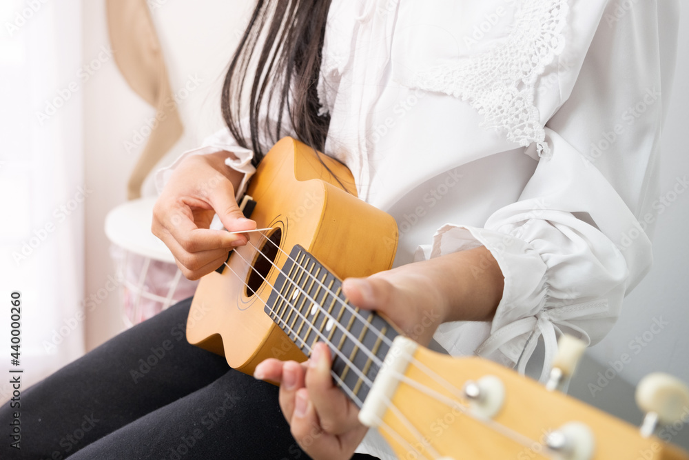 Asian child girl is playing a wooden ukulele