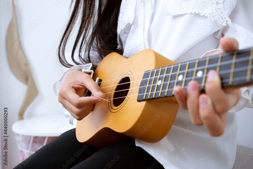 Asian child girl is playing a wooden ukulele