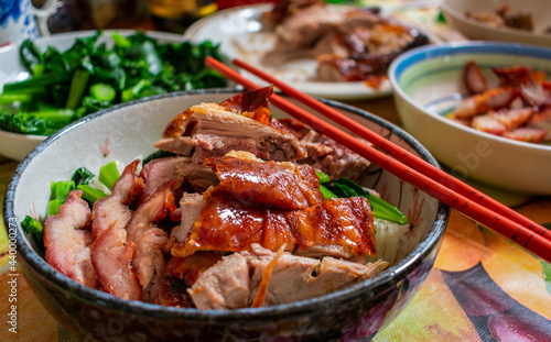 Cantonese roast duck, honey roast pork with vegetables and rice in a bow.