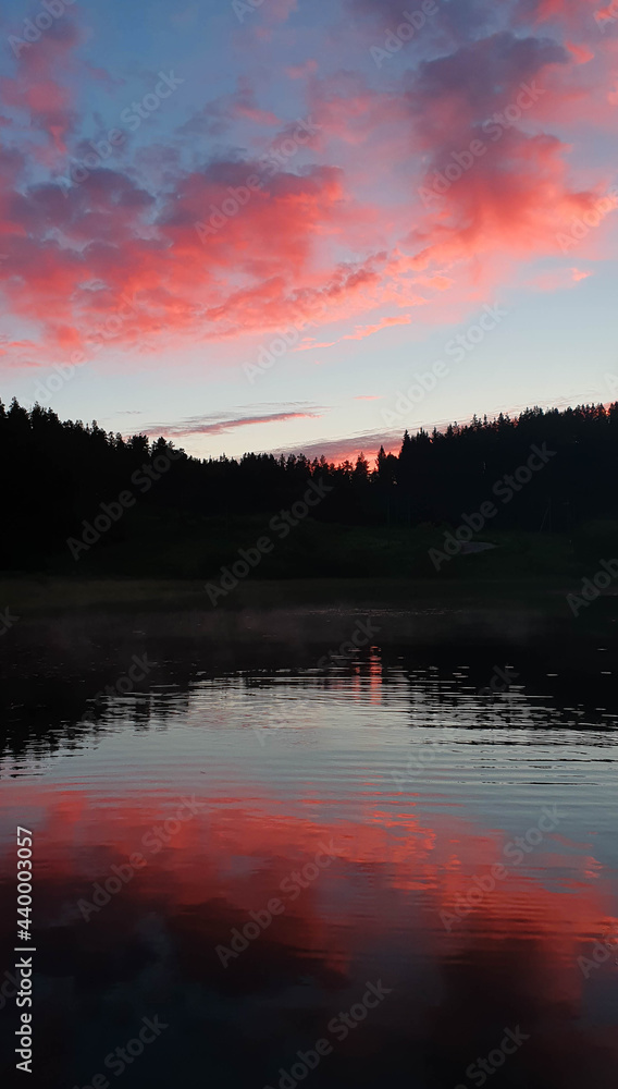 Colorful sunrise with cirrus red clouds on forest lake in Karelia, Russia. Natural landscape, vertical photo. High quality photo