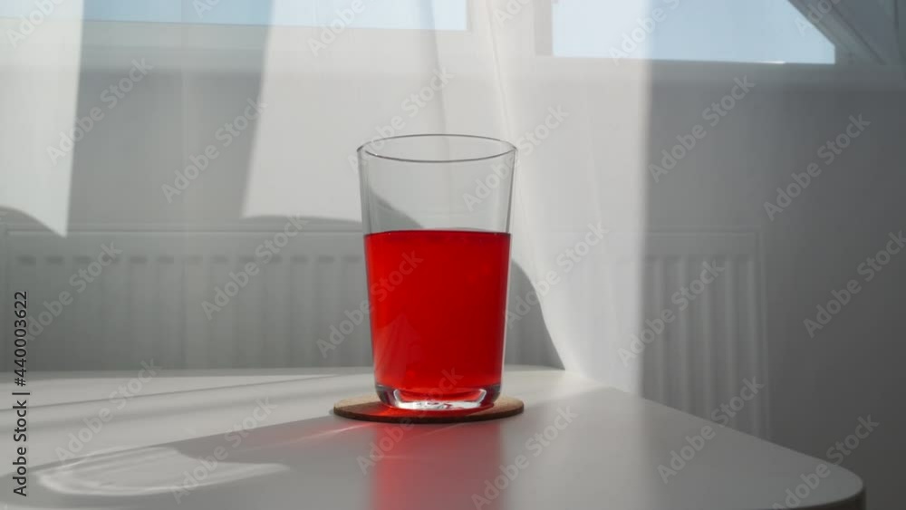 Glass with fresh strawberry lemonade in sunlight from window with transparent white curtain, homemade refreshing cold red fruit drink closeup. High quality 4k footage Glass with fresh strawberry lemonade in sunlight from window with transparent white curtain, homemade refreshing cold red fruit drink closeup. High quality 4k footage