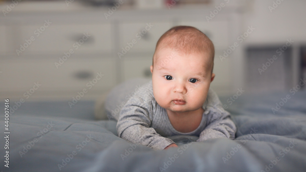 Cute bald baby 2 3 months old lies on the bed on his stomach, close-up, toning Cute bald baby 2 3 months old lies on the bed on his stomach, close-up, toning