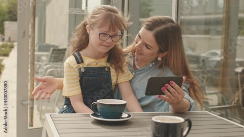 Wallpaper Mural Medium slowmo of affectionate young woman and her 11-year-old daughter with down syndrome video chatting on smartphone while sitting outside cafe on sunny day Torontodigital.ca