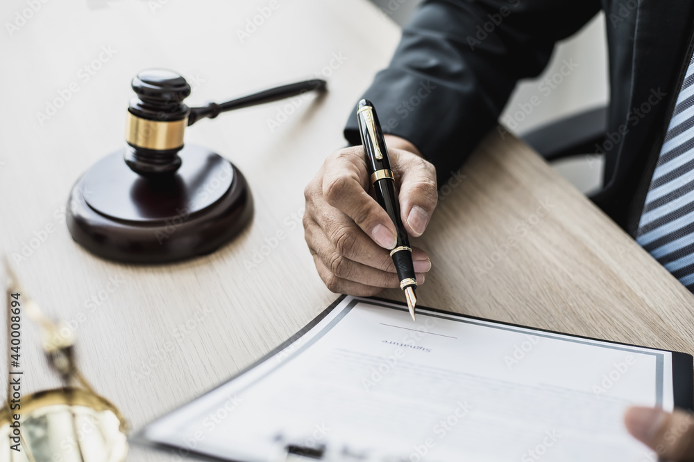 Attorney at work, on the table there is a small hammer to beat the judges table in court. and justice scales, lawyers are drafting a contract for the client to use with the defendant to sign. Attorney at work, on the table there is a small hammer to beat the judges table in court. and justice scales, lawyers are drafting a contract for the client to use with the defendant to sign.