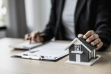 Small gray house model is an example of a house in a housing project, the house salesperson checks the contract documents before meeting the customer. Real estate leasing concept.