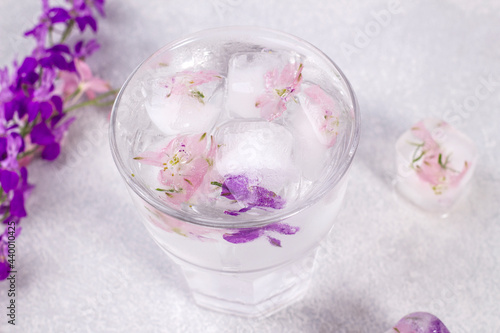 Glass with lemonade and ice cubes with purple and soft pink flowers